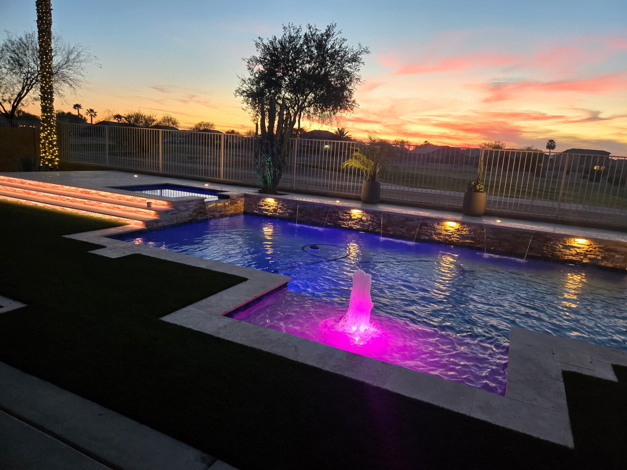 Custom pool at sunset with a lit fountain, stone scupper wall and raised spa